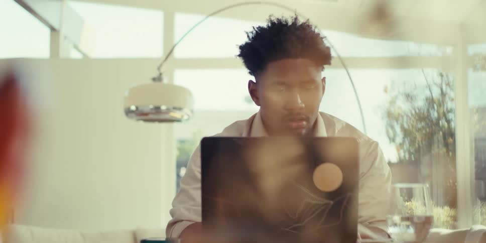 A man in a shirt works on a laptop and uses a smartphone while sitting at his desk