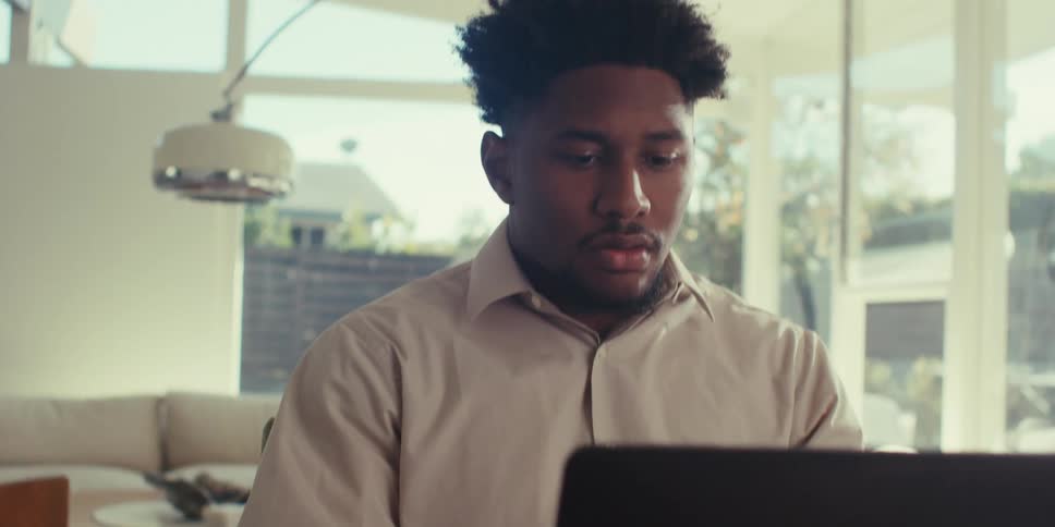 Man in a brown shirt sitting at a brown table uses a laptop in the living room