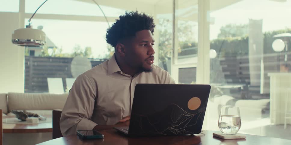 A man sits in his home thinking in depth about something with a laptop computer in front of him