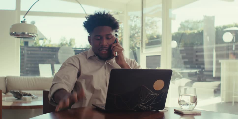Man working on a laptop and then answering a call on his smartphone