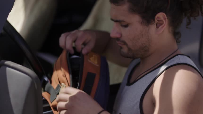 Man putting items into a small carrying bag and then leaving them beside his car