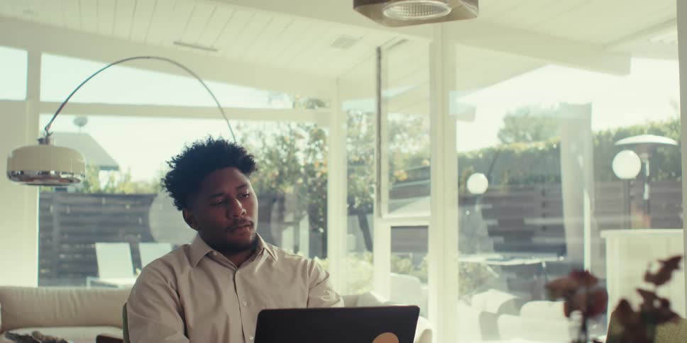 Man with short beard works concentrated on a laptop inside a house