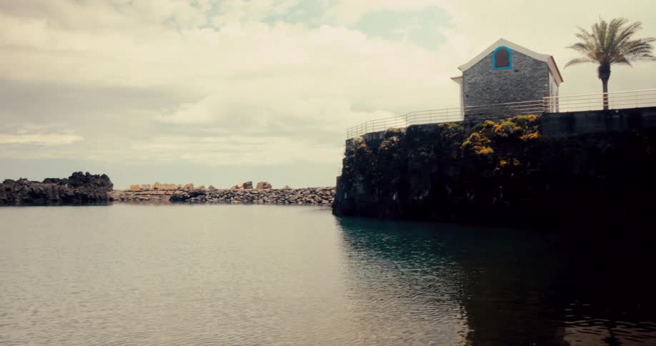 Small buildings on the edge of a lake surrounded by rocks and the ocean in the background