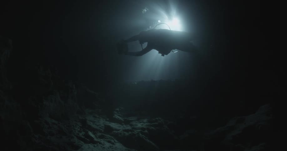 A scuba diver swims underwater in the dark with a camera