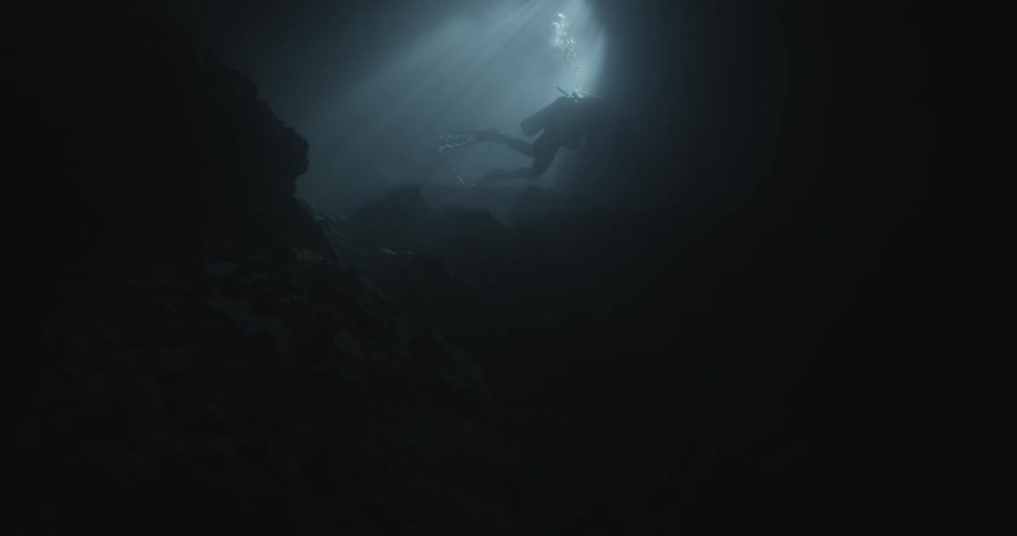 A scuba diver is exploring an underwater scene while sunlight streams down into the water