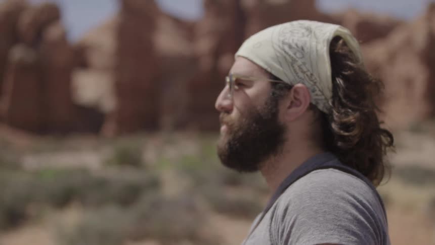 A man with a bandana on his head stands in the desert