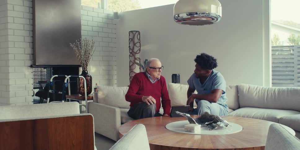 Elderly man talking to a young man sitting in a living room
