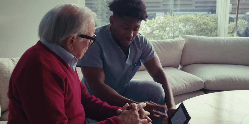 A healthcare worker is talking with a man while pointing towards a tablet