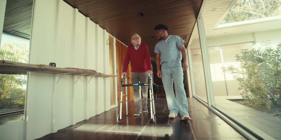 A health worker walks with an elderly man as he uses a mobility walker