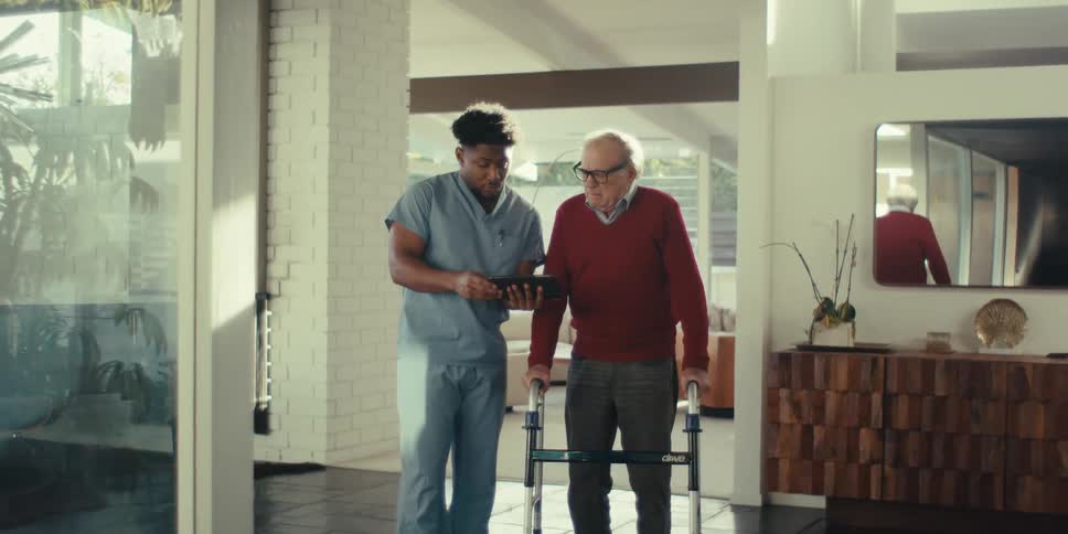 Nurse standing next to an elderly man presenting something to him on a tablet