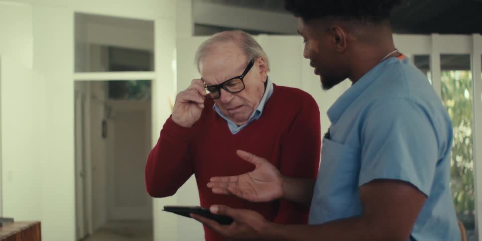 Elderly man putting on glasses and talking to a nurse next to him