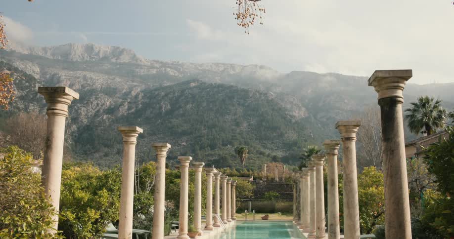 Swimming pool surrounded by classical columns and mountains in the background