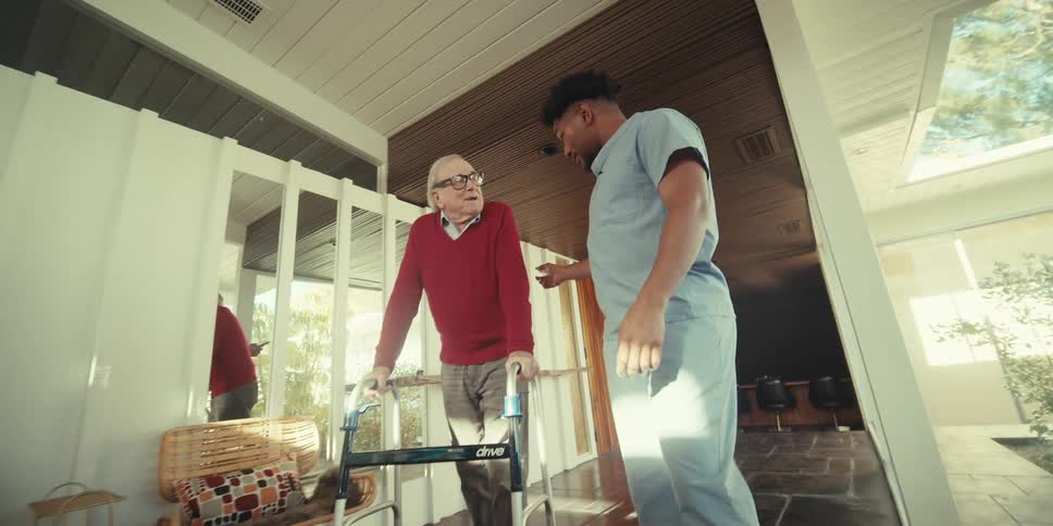 Elderly man walking with a walker next to a nurse