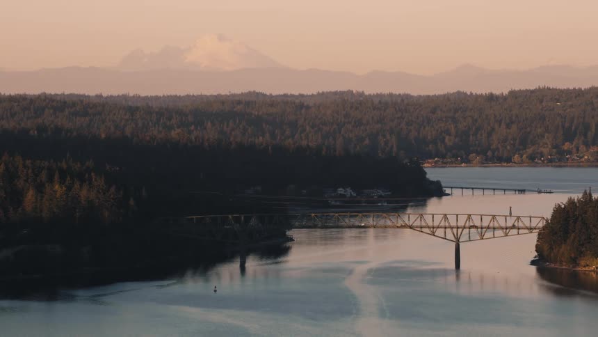 Aerial view at sunrise of a bridge over a sea channel surrounded by forest
