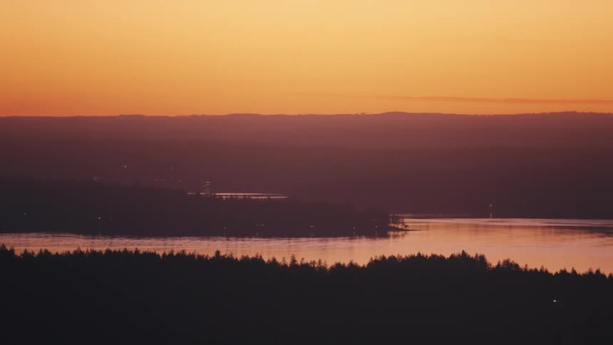 Water flowing past forested shores reflects a red sky