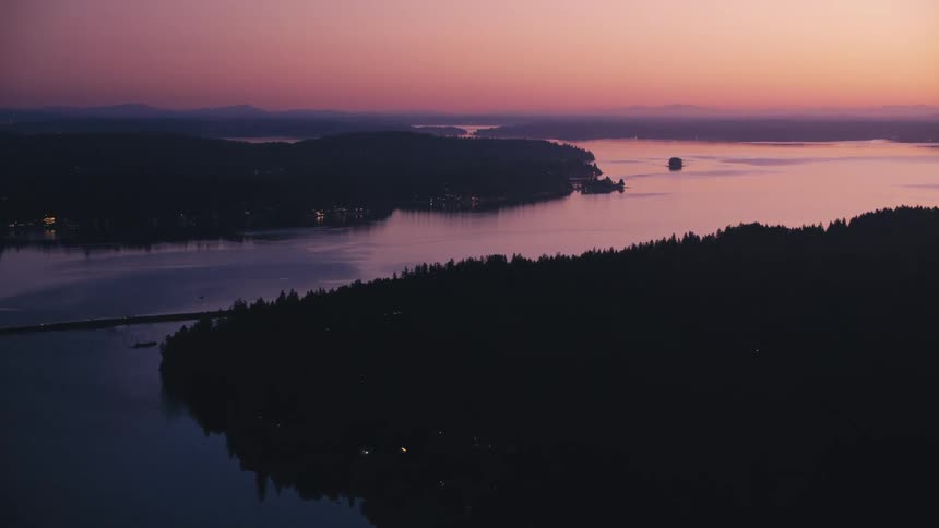 A dusky pink sky frames a dark silhouette of forested hills surrounding a calm winding river