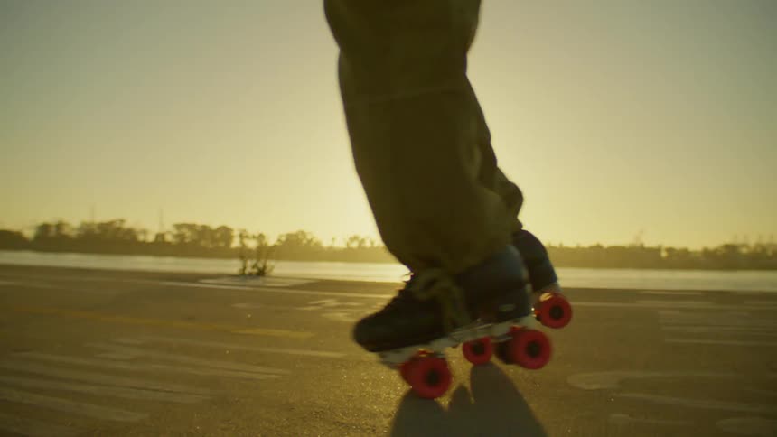 A dancer performs a spinning dance move on roller skates near a waterfront at sunset