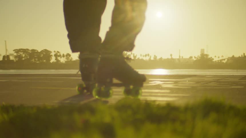 A person is roller skating on a paved surface near a body of water with palm trees in the background during sunset