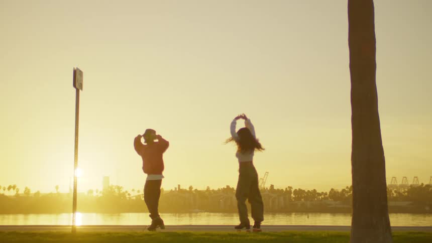 Two people spin in roller skates by the shore at sunrise