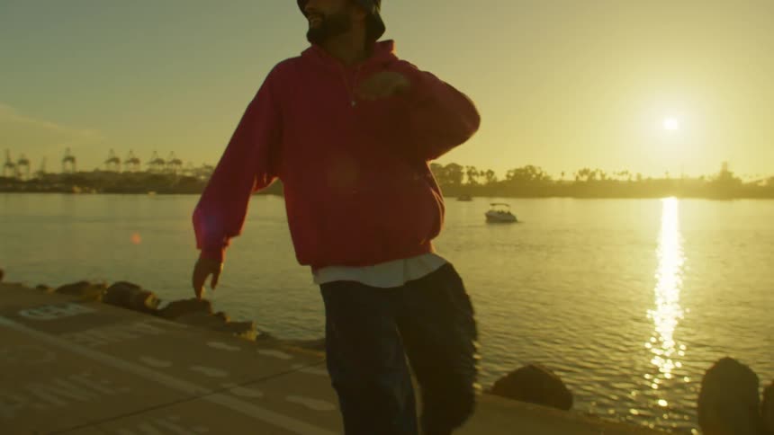 Man dancing on roller skates by a lake with the sunset on the horizon