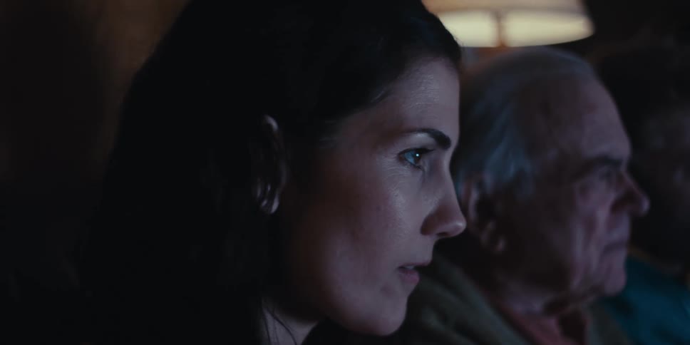A family of three is sitting on a couch in a dimly lit room watching television together