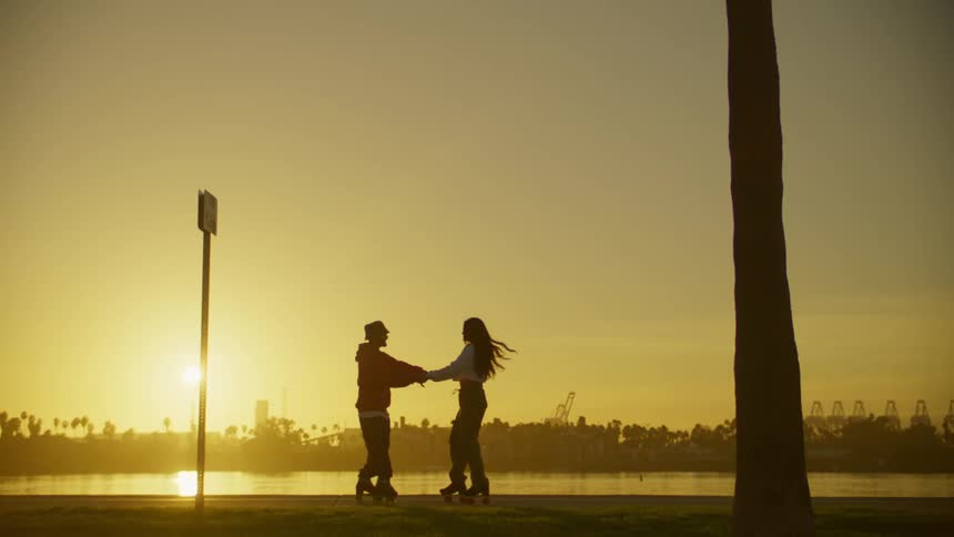 Silhouette of two people dancing on roller skates by a lake at sunset