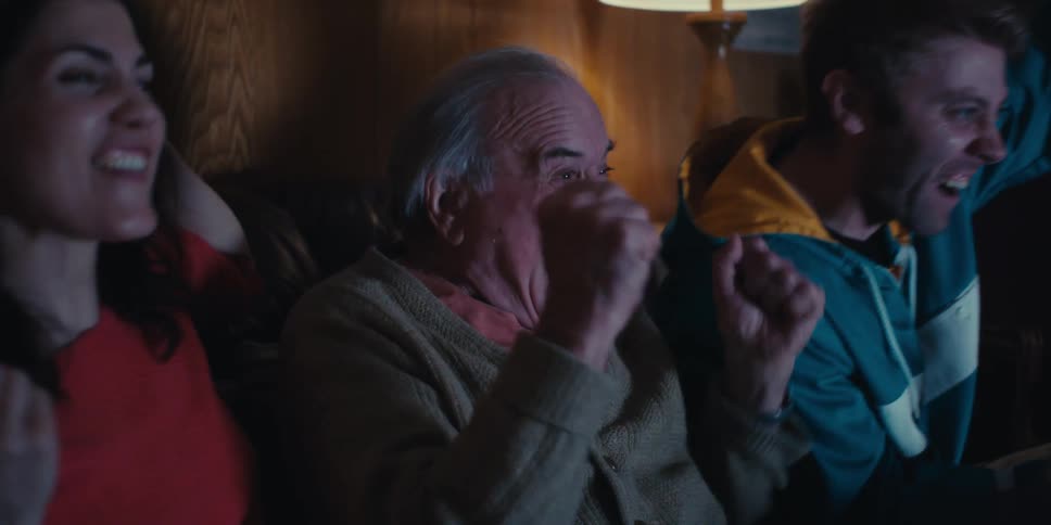 Three people sitting on the couch happily cheering while watching something