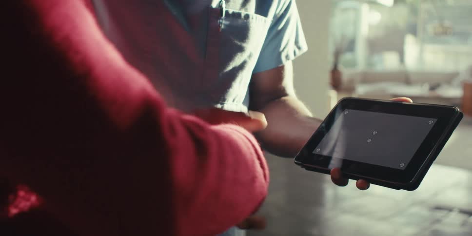 Two individuals shake hands with one person holding a tablet and the other reaching for the handshake