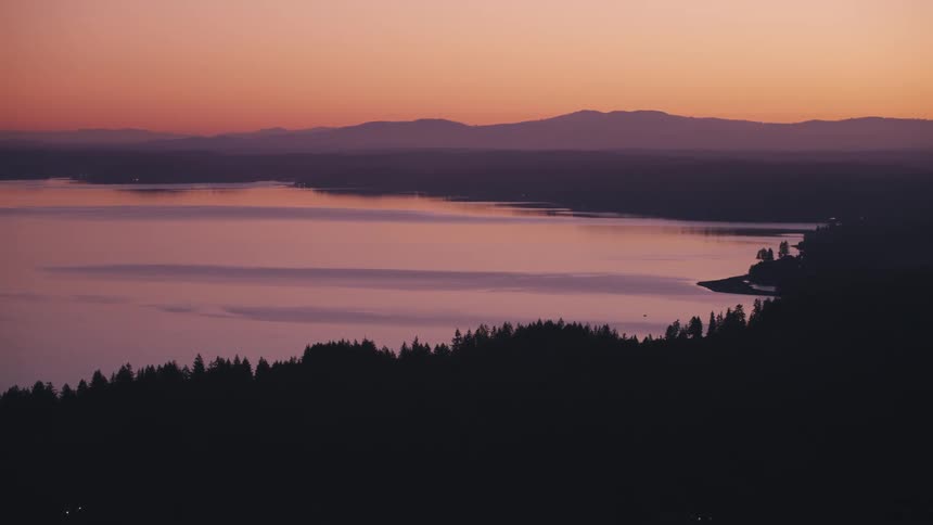 Aerial panorama of a silhouette of a forest surrounded by a lake