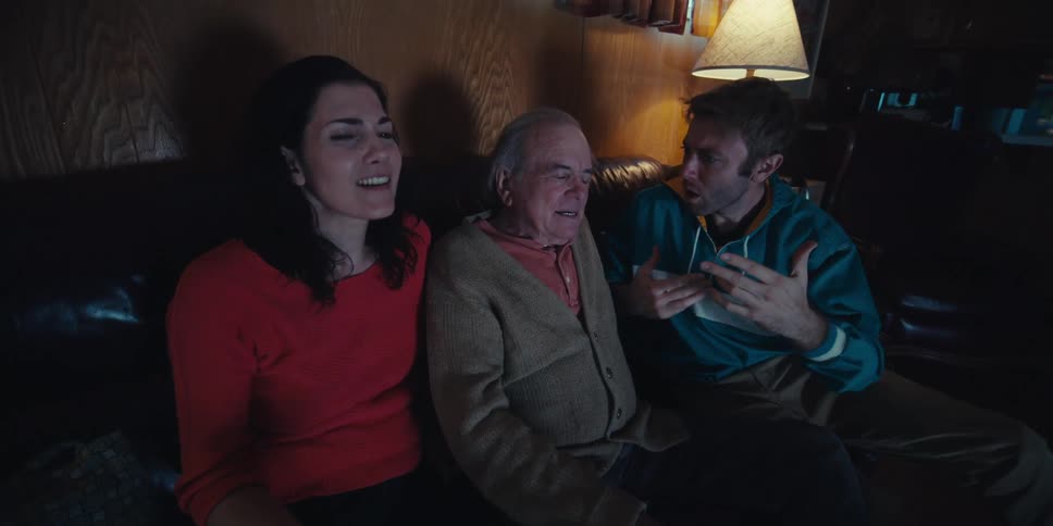 Elderly man sitting in the middle of two young adults happily watching something
