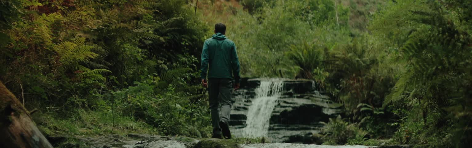 Man walking near a small waterfall in a forest
