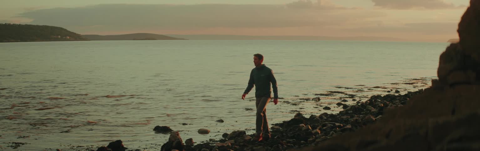 Man walking on rocks by the sea at dawn