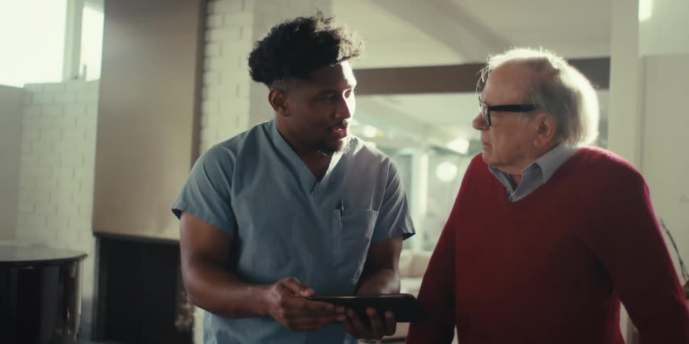 A healthcare worker is talking with a patient and using a tablet