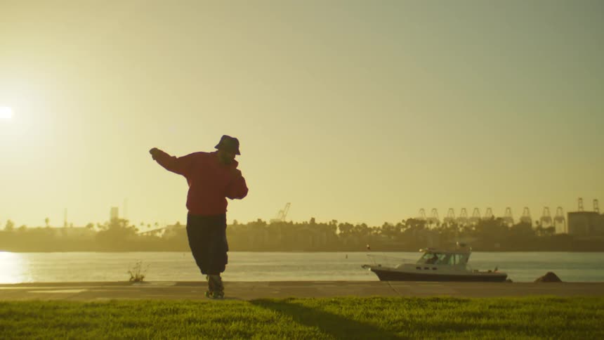 A person is roller skating on a paved surface near a body of water with palm trees in the background during sunset