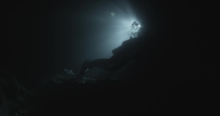 A scuba diver swims in the dark water