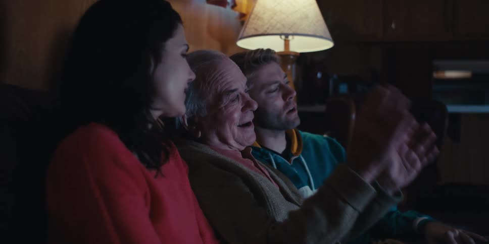 Elderly man sitting between two young adults on a sofa in the living room