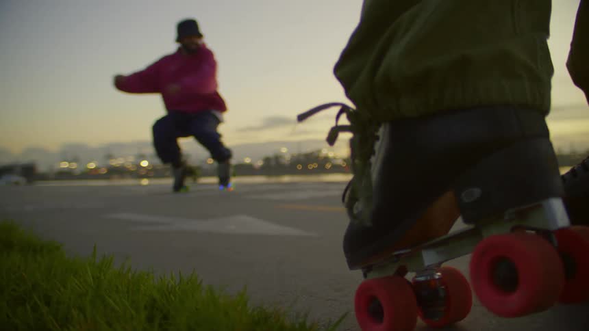 A couple of dancers perform energetic dance moves on roller blades near a waterfront at sunset