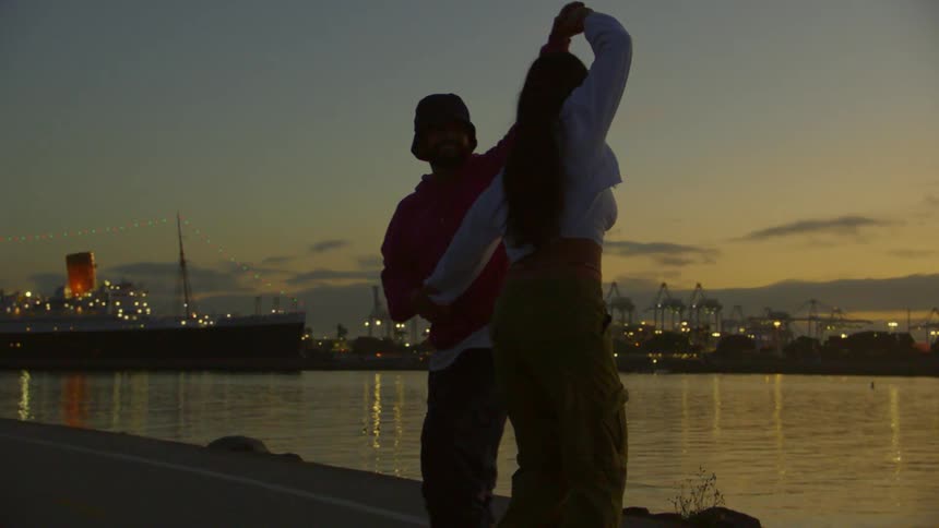 Man and a woman on roller skates dancing together by a lake at dusk