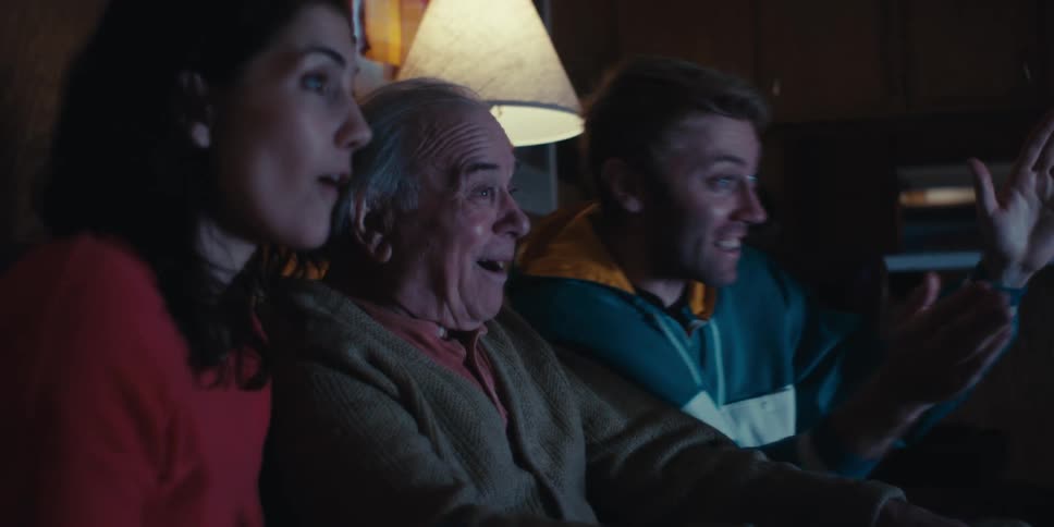 Elderly man and two young adults sitting on the couch watching and enjoying together