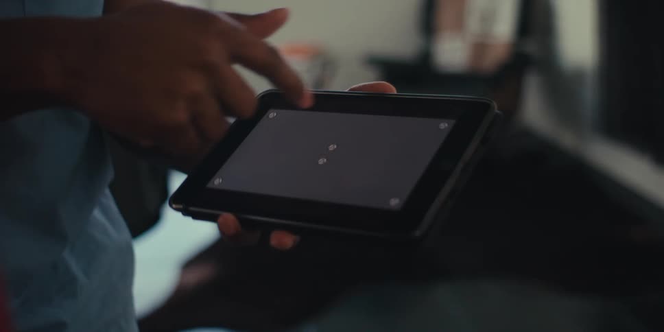 Closeup of a hand holding a tablet with a gray screen while another finger points at it