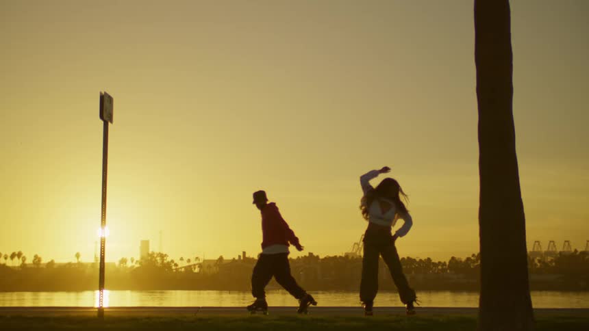Woman and a man dancing on roller skates by a lake at sunset