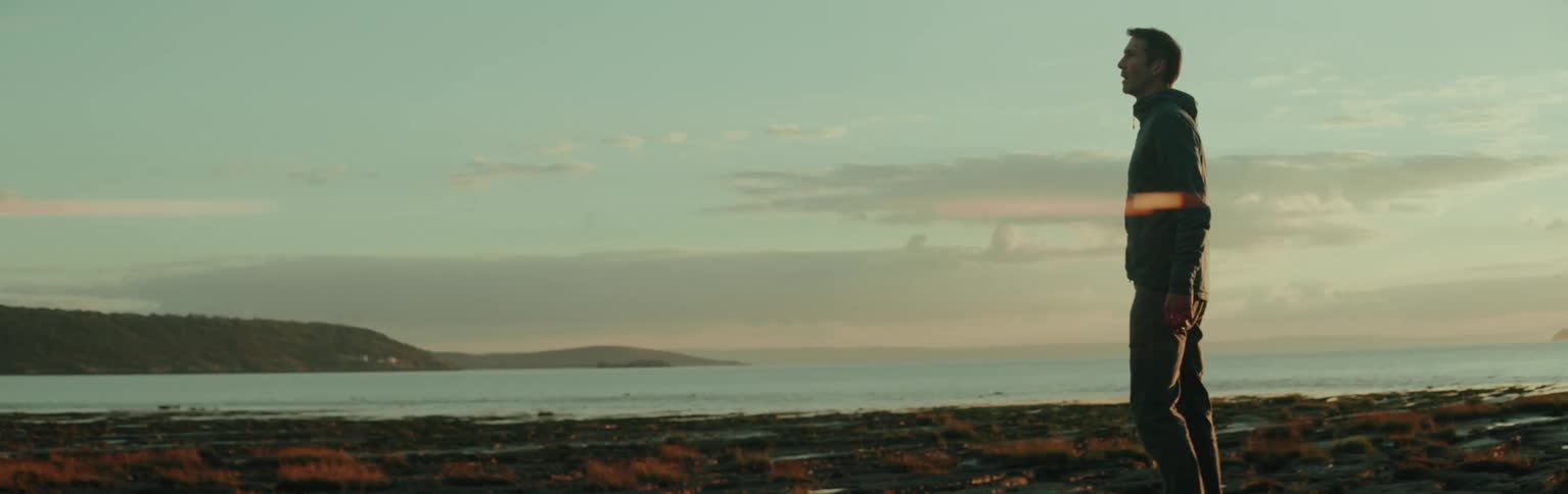 A man stans in the coast next to the ocean at sunset