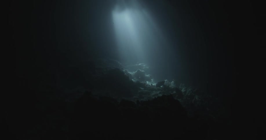 A beam of light hits the rocks deep underwater