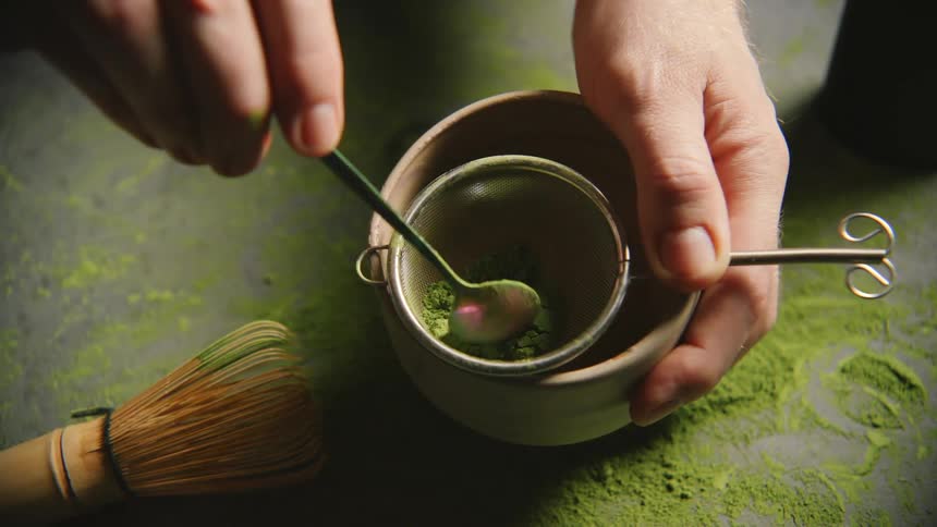 Hand holding a mug and preparing green tea