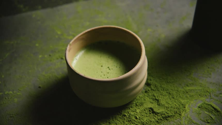 Hand picking up green tea in a mug on top of a table with powder