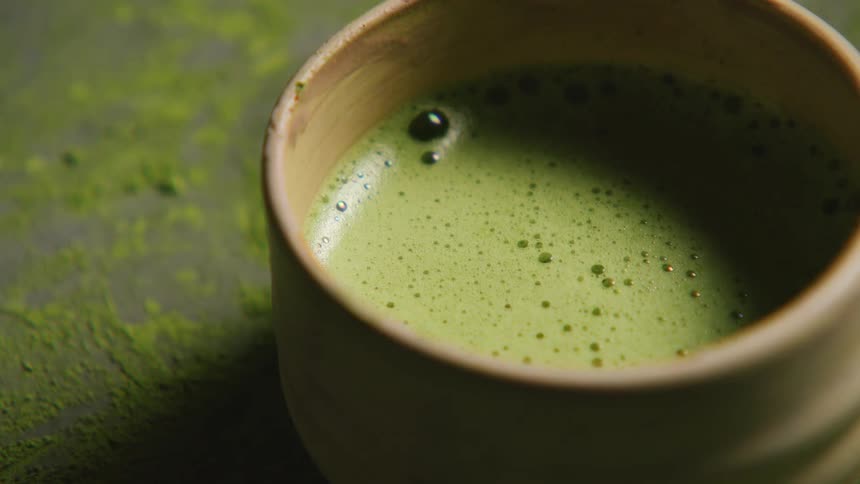 A closeup view of a ceramic cup filled with frothy green matcha tea with some bubbles visible on the surface