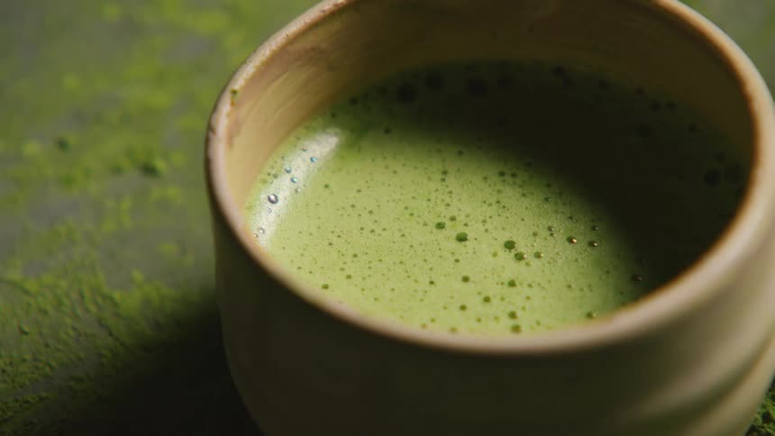 A person lifts up and puts down a cup of green drink