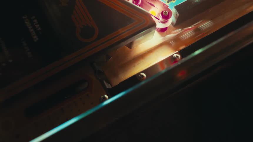 Chrome ball reflects amber light as it slides along the metal track of a retro pinball machine