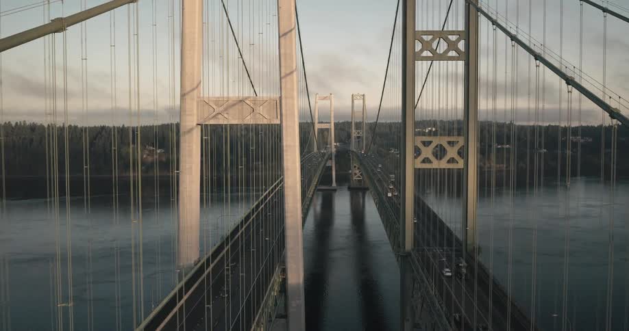 Grand suspension bridge reflects the soft light of dawn as it stretches over the calm waters of the river