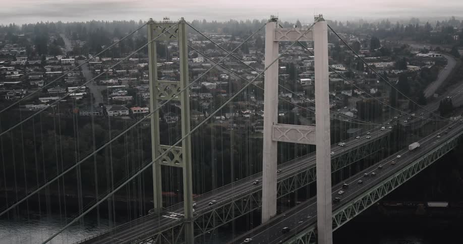 Towering suspension bridge spans a serene river connecting a fogshrouded city to a busy highway